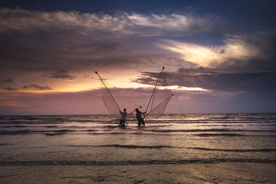 Silhouette people on beach against sky during sunset