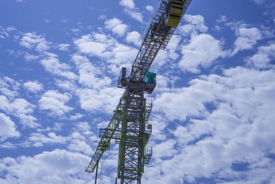 Upward view of a large heavy tower crane, long silver and green color on steel beam arm 