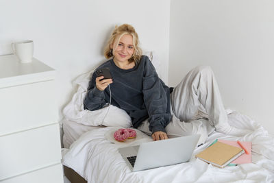 Portrait of young woman sitting on bed at home