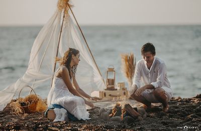 People sitting on beach by sea against sky