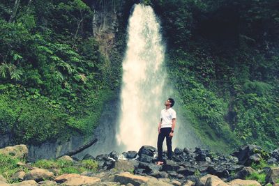 Low angle view of man standing by waterfall in forest