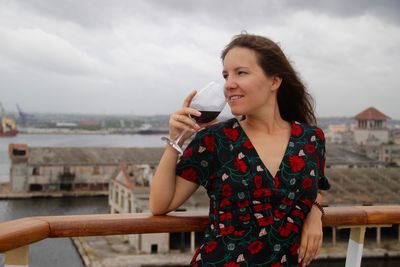 Young woman drinking wine while leaning on railing