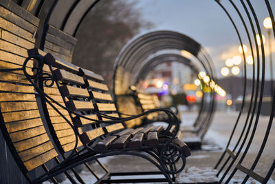 Wooden benches in lantern light in city park. people walking down by alley. evening winter 