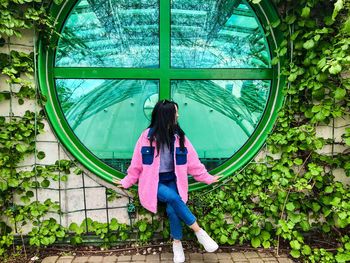 Young lady in pink jacket at the rooftop of warsaw university library near green round window 