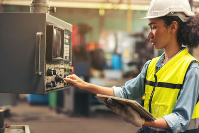 Standing in front of a control panel, a female industrial electrical engineer with a safety .