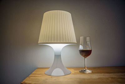 Illuminated lamp on table against wall at home
