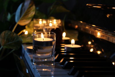 Lit tea light candle on piano at night