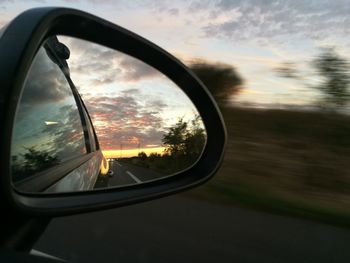 Close-up of side-view mirror against sky