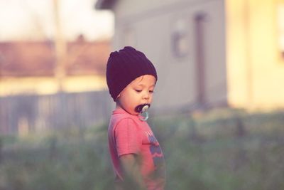 Close-up of baby boy with pacifier in mouth standing amidst plants at park