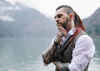 A brutal male hipster groom in a wedding suit in nature by the mountains and lake