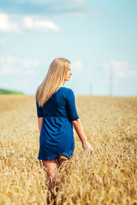 Rear view of young woman walking on wheat field against sky