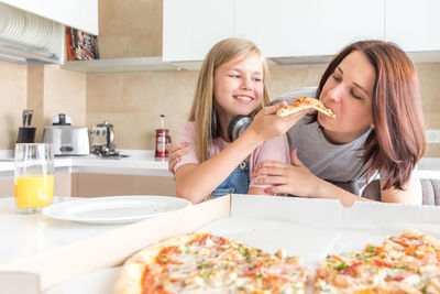 Daughter feeding pizza to mother at home