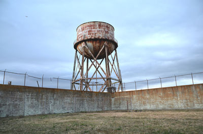 Old rusty metallic water tank by surrounding wall against sky