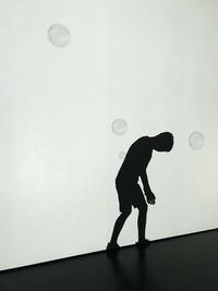 Side view of silhouette man playing with ball against wall