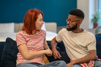 Young interracial couple husband and wife sit on bed at home discussing intimacy issues