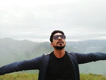 Young man wearing sunglasses standing against mountain range