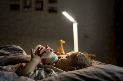 Baby boy drinking milk from bottle lying on bed