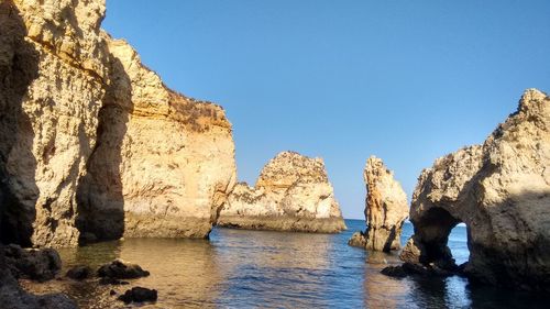 Panoramic view of rock formations in sea against clear blue sky