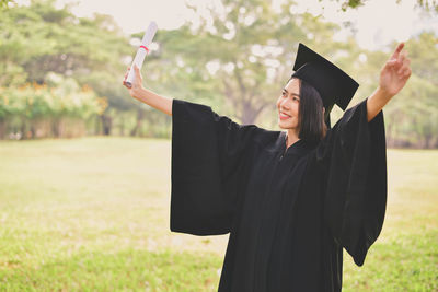 Young woman in graduation gown looking away while standing at park