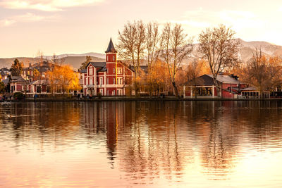 House by lake and buildings against sky