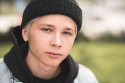 Stylish teen boy 15-16 year old wearing black knitted hat and hoodie outdoors close up. 