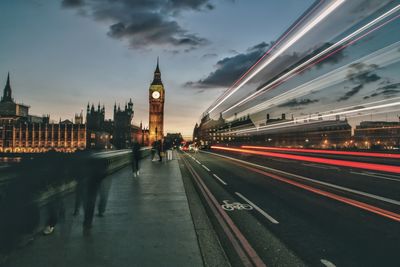 Light trails on road against big ben during sunset in city