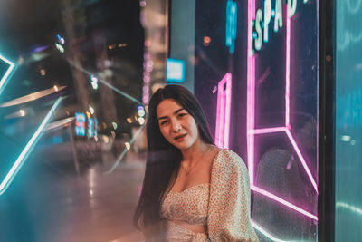 Portrait of woman standing by illuminated store at night