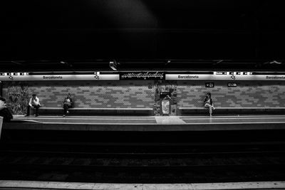 People waiting at railroad station platform at night