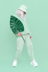 Full length of woman holding leaf while standing over green background