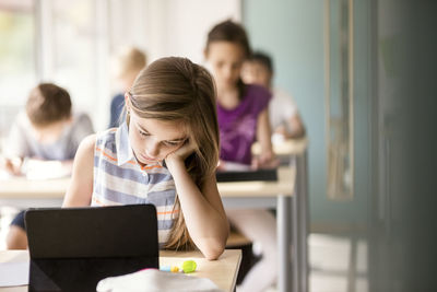 Schoolgirl studying at desk with students in classroom