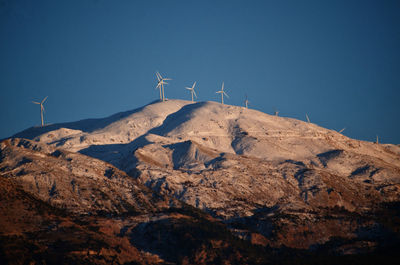 Scenic view of snowcapped mountain and wind turbines against clear sky