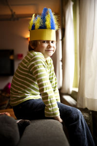 Side view portrait of smiling boy wearing feather hat at home