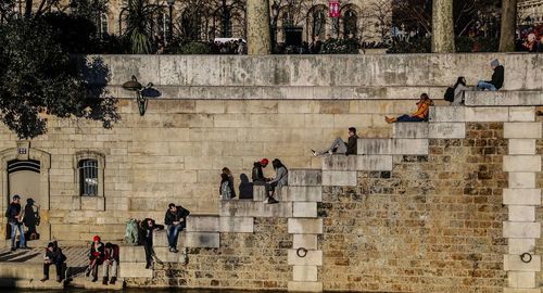 People sitting on staircases against buildings in city