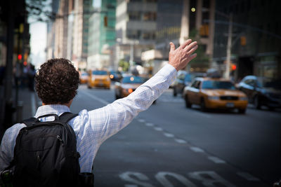 Rear view of man waving hand while standing on city street