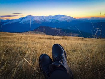 Black boots and snowcapped mountains in the background at sunset