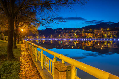 Illuminated footpath by lake against sky at night