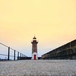 Lighthouse by sea against sky during sunset