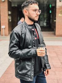 Man holding disposable cup while standing on footpath in city