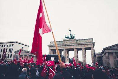 People in front of flags against sky in city