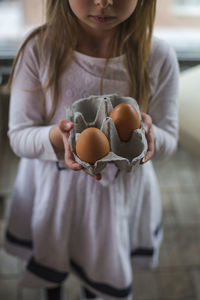Midsection of girl holding eggs at home
