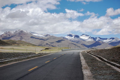 A flat newly built unmanned asphalt road leads to the foot of the snowy mountain ahead