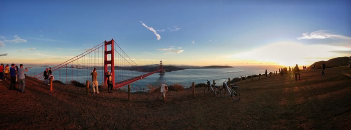 People at beach against bridge during sunset