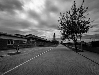 Street by footpath against sky in city