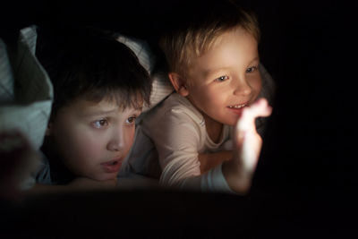 Cute smiling brothers on bed watching movie at night