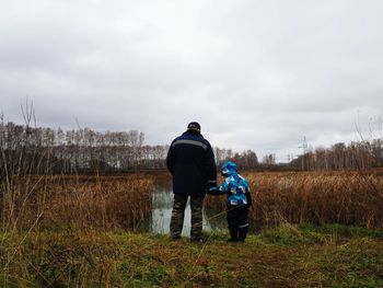 Rear view of man and child on field against sky