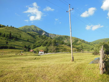 Electric pole on green landscape by mountain against sky