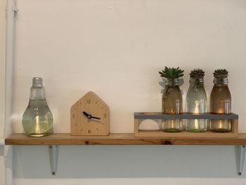 Empty glass bottles on table against wall at home