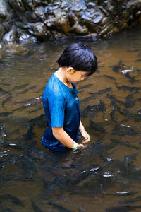 An asian boy feed and play with kelah fish in kelah sanctuary kenyir lake, terengganu.