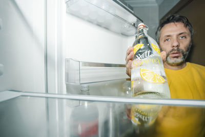 Middle-aged man with beard at the empty fridge with one bottle of water