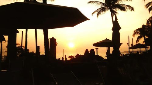 Silhouette palm trees by swimming pool against sky during sunset